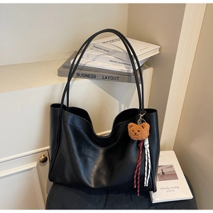 Detail of a black faux leather tote bag with a cute brown plush bear charm and woven cord