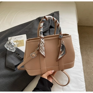 Detailed view of apricot textured leather bucket bag with decorative silk scarf on handle