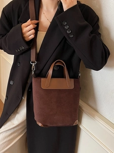 Dark brown suede bucket bag with leather handle and wide strap on a female model