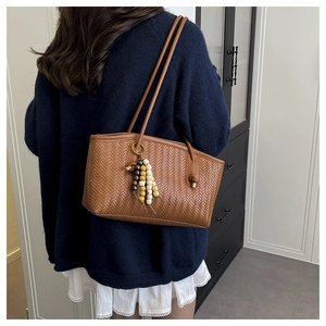 Detail of a brown woven tote bag with herringbone pattern and beaded tassel pendant