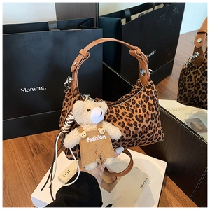 Detail of leopard print handbag with brown leather handle and cute plush bear charm