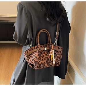 Detail of leopard print bucket bag with brown leather handles and a beaded charm on a model