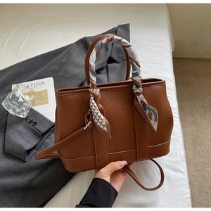 Detail of brown litchi pattern leather tote bag with decorative blue patterned silk scarf