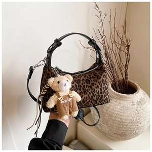 Detail of leopard print handbag with black leather handle and plush bear charm