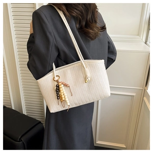 Detail of white tote bag with V-shaped woven texture, beaded charm and leather handle