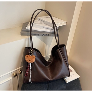 Detail view of dark brown faux leather tote bag with plush bear charm and natural texture