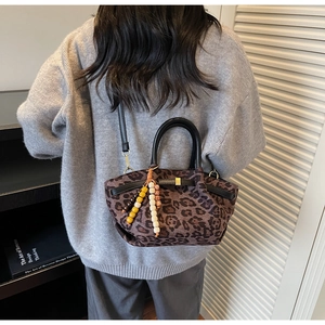 Detail of leopard print bucket bag with wooden bead charm and black leather handle