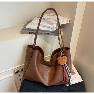 Detail of dark brown leather tote bag with plush bear charm and woven rope decoration