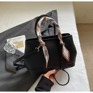 Detail of black lychee-textured handbag with decorative silk scarf on the handle