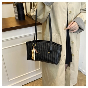 Detail shot of a black woven tote bag with wooden bead charm on a slim shoulder strap