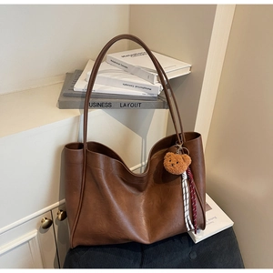 Detail of dark brown tote bag with vintage leather texture and cute plush bear charm