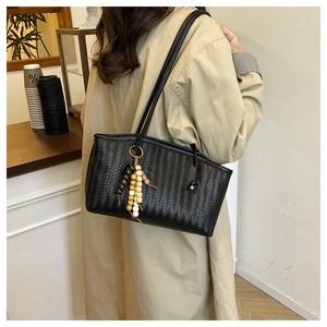 Detail of black woven leather tote bag with boho bead charm in a minimalist cafe setting