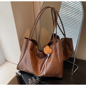 Detail view of large brown tote bag with cute teddy bear charm and soft leather texture