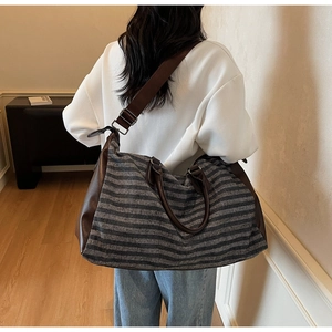 Detail of a large striped canvas travel bag with leather accents shown on a model