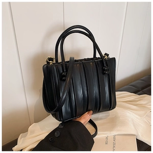 Detail of black pleated tote bag showing vertical texture and gold hardware accents