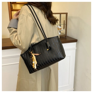 Detail of black woven tote bag with fringe charm worn over the shoulder by a model