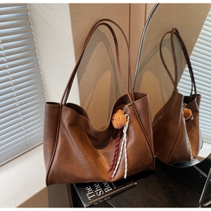 Detail view of brown leather tote bag with plush bear charm and woven rope accessory