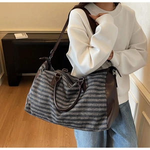 Detailed view of striped travel duffel bag with leather trim on model indoors