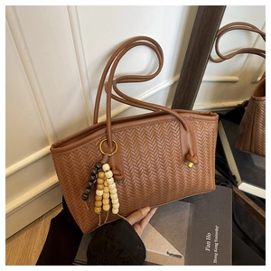 Detail of brown woven tote bag with V-shaped texture and wooden bead tassel accessory