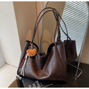 Detail of dark brown tote bag with plush bear charm and woven rope accessory