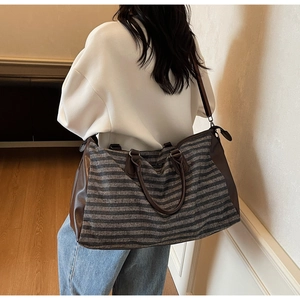 Side view of large striped travel bag with leather accents shown on a model
