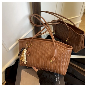 Close-up of brown woven tote bag featuring beaded charm and leather knotted shoulder strap