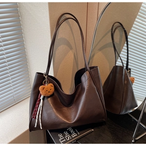 Detail of dark brown leather tote bag with plush bear charm and woven rope accent