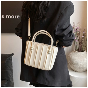 Detail of a creamy white pleated tote bag with cylindrical knots and adjustable strap
