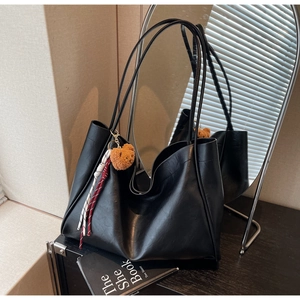 Detail of large black tote bag with leather texture and cute bear pendant accessory