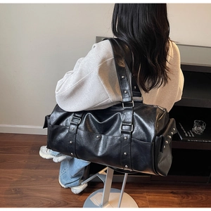 Close-up of black grainy leather duffel bag featuring silver studs and wide shoulder strap