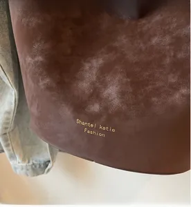 Detail der matten Textur und des goldenen Markenlogos an einer braunen Handtasche