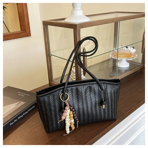 Detailed view of black woven tote bag with leather texture and colorful wooden bead tassel
