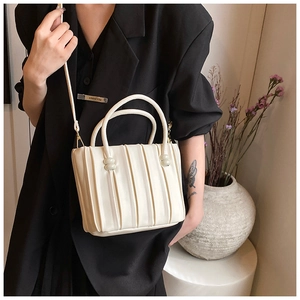 Detail of white pleated leather tote bag with bead accents and thin crossbody strap
