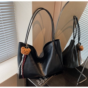 Detail of black Hobo tote bag with slim shoulder straps and cute plush bear charm accessory