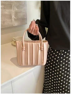 Detail of light pink pleated bucket bag with ball-shaped accents and elegant top handle