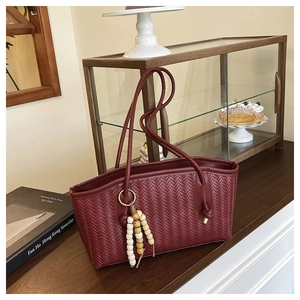 Detail of dark red woven tote bag featuring a wooden bead tassel and textured finish
