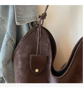 Detailansicht der braunen Wildledertasche mit goldenem Druckknopf und Knotendetail am Gurt