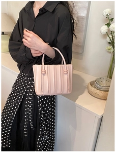 Close-up of pink bucket bag featuring pleated leather texture and gold sphere handle detail
