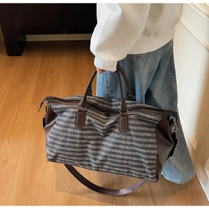Detail of grey striped travel duffel bag with brown leather handles and adjustable shoulder strap