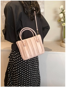 Detail of light pink pleated bucket bag worn by model showing vertical texture and strap