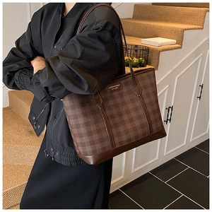 Detail shot of a dark brown checkered tote bag with a leather brand tag and straps