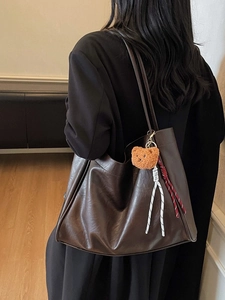 Deep brown retro leather tote bag with plush bear charm and woven straps on model shoulder