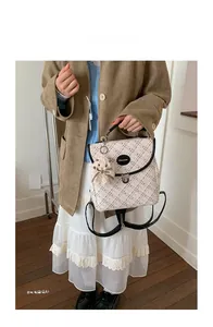 Close-up of cream plaid backpack featuring black trim and a cute plush bear charm accessory