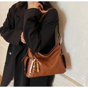 Detail view of large brown crossbody bag with wooden bead tassels and side pocket