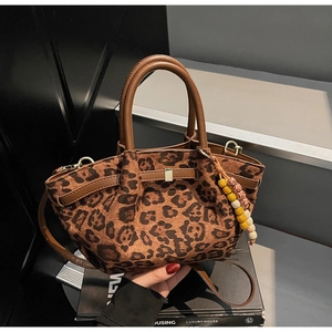 Detail of leopard print bucket bag featuring brown handles and colorful beaded charm accessory
