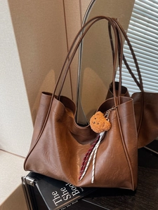 Retro deep brown leather tote bag with plush bear charm in a minimalist studio setting