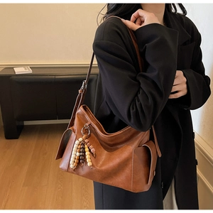 Detail of vintage brown leather bag with side pocket and decorative wooden bead tassel