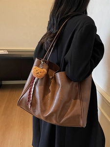 Elegant brown leather tote bag with small bear pendant shown on model in warm lighting
