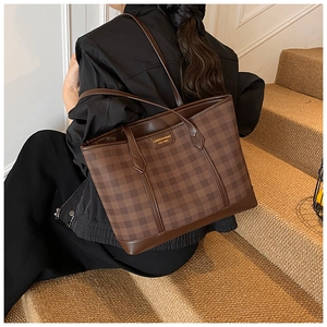 Close-up of brown checkered tote bag with gold logo plaque and leather shoulder strap