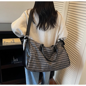 Detailed view of striped travel bag with black leather trim and adjustable shoulder strap